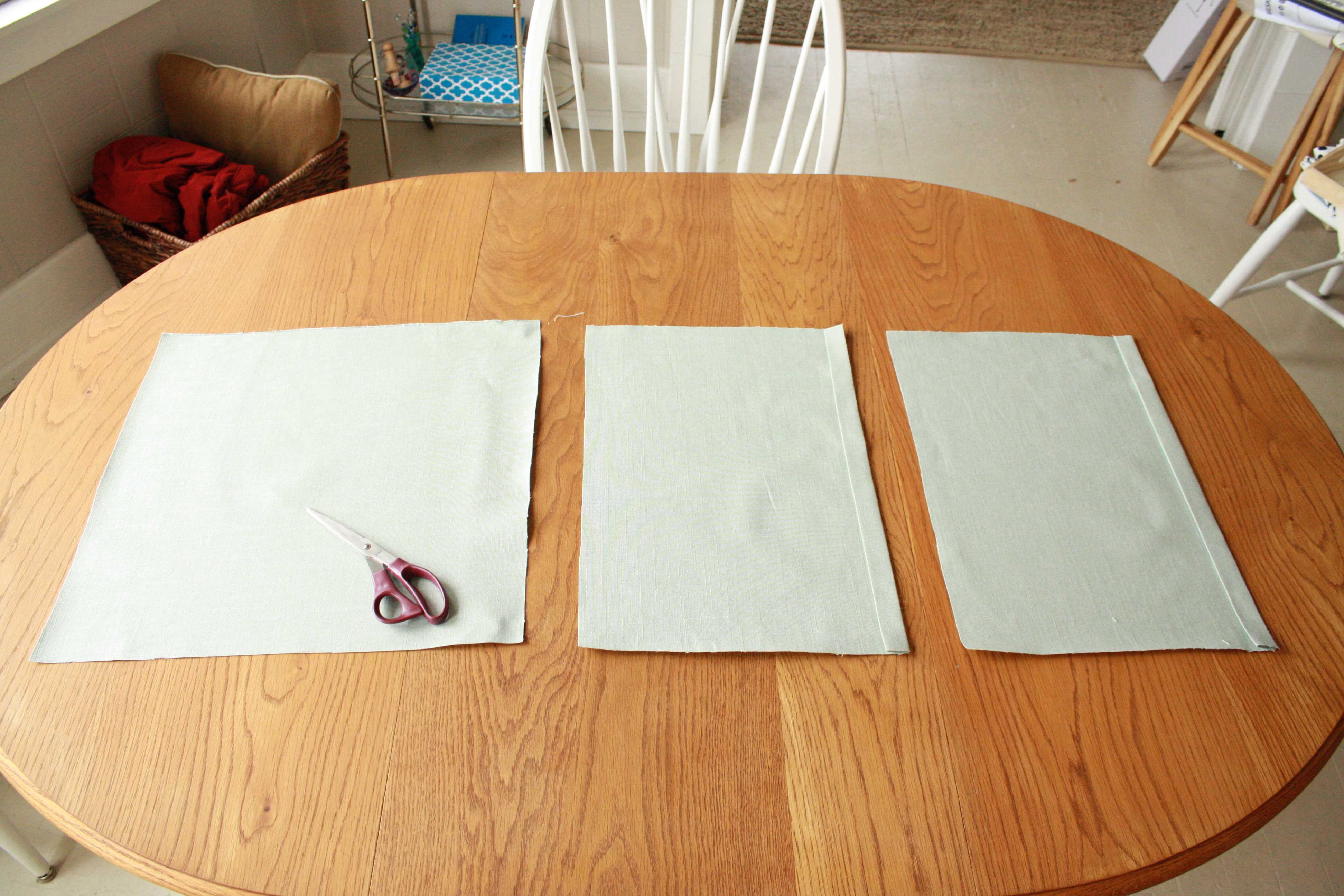Pale green fabric pieces laid on a round wooden table with scissors, evoking a calm creative workspace